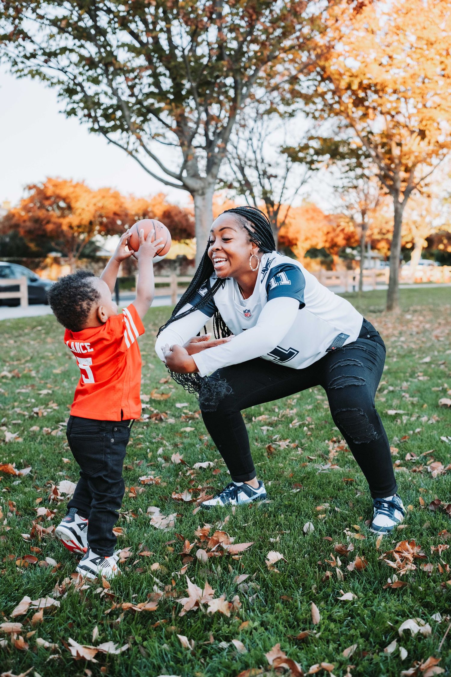 A joyful moment captured outdoors during autumn as parent and child play together among fallen leaves in a park.