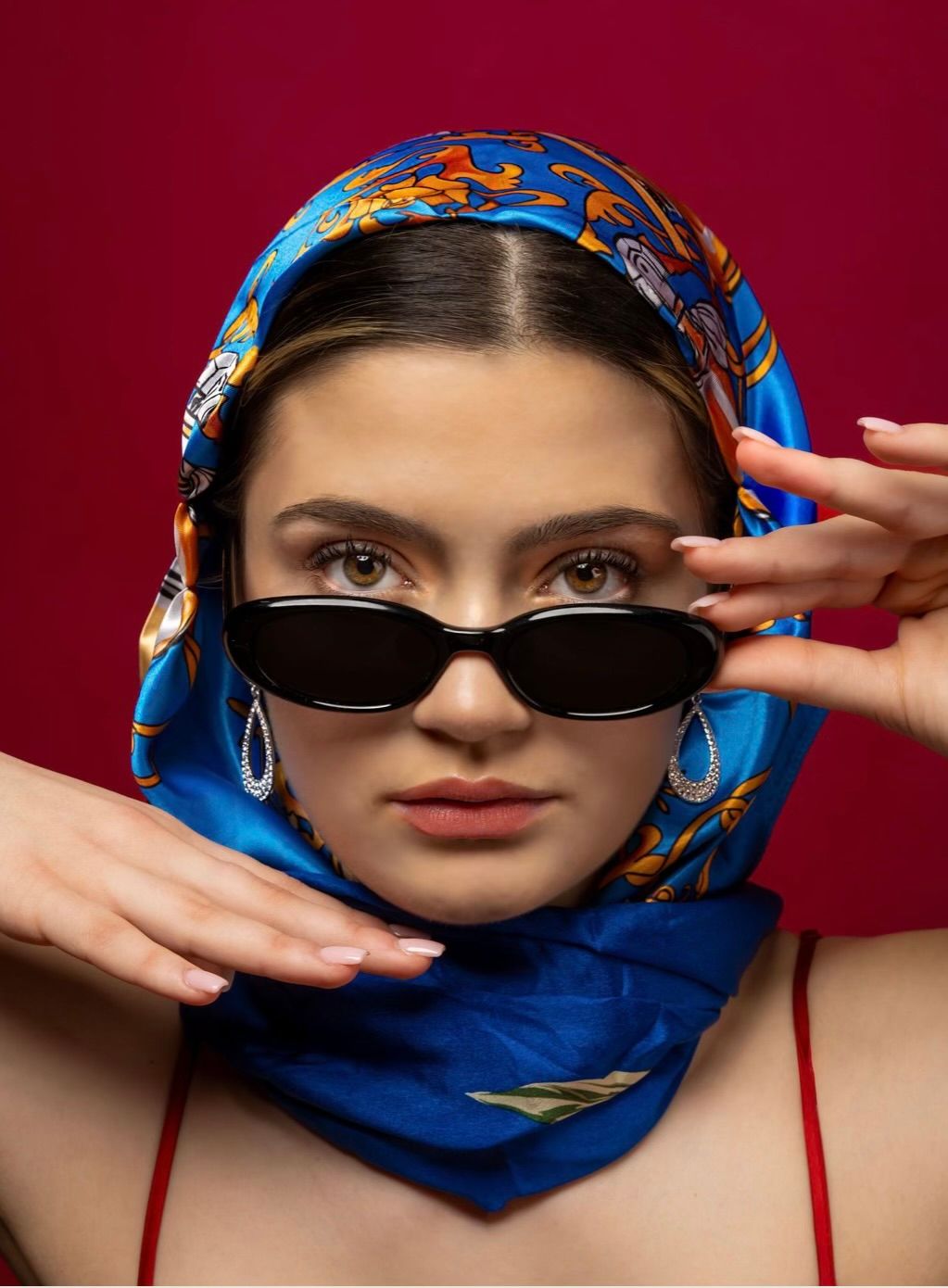 Red backdrop with a girl in a red dress and a blue head scarf, looking straight to the camera