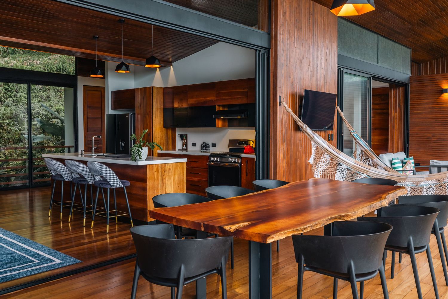 Modern wooden dining room with large windows, live edge table, and black chairs in an open concept space.