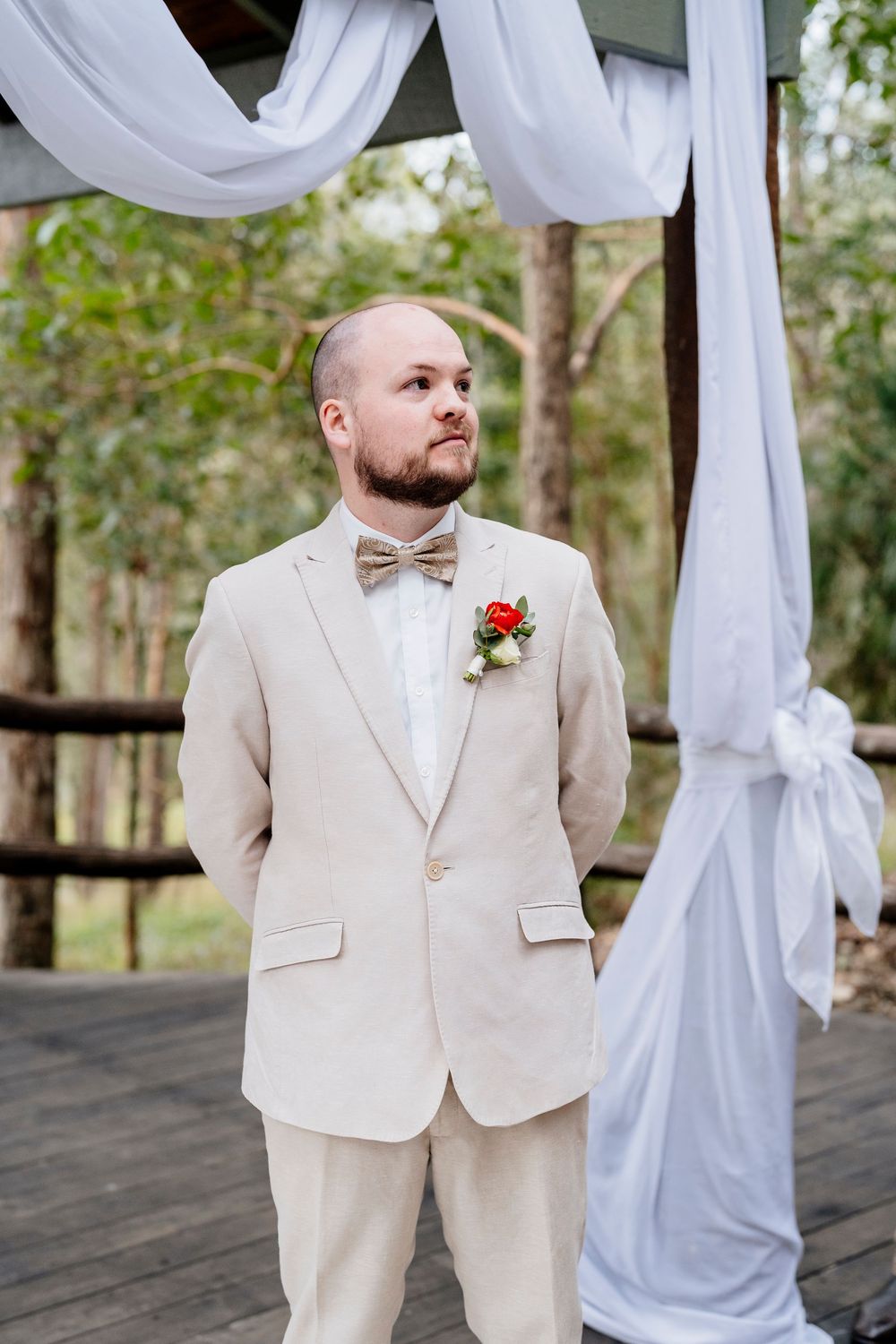 Wedding ceremony setup on wooden deck with white draping and natural forest backdrop.