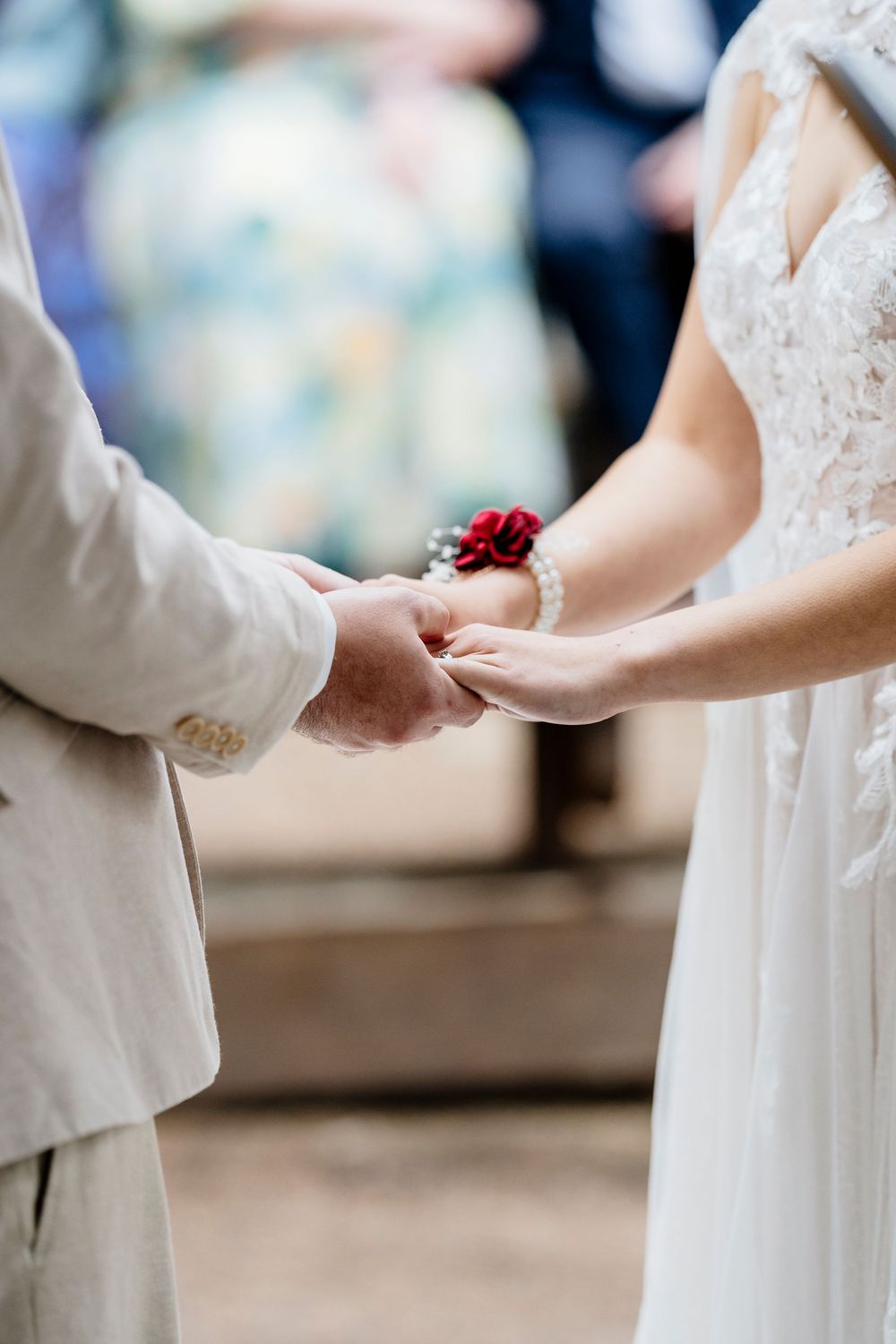 Close-up view of two hands holding each other during a wedding ceremony, with white dress details visible.