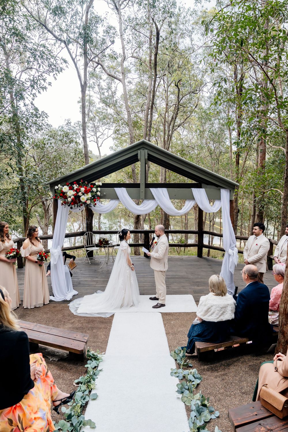 Outdoor wedding ceremony in a rustic wooden pavilion decorated with flowing white fabric and floral arrangements at walkabout creek
