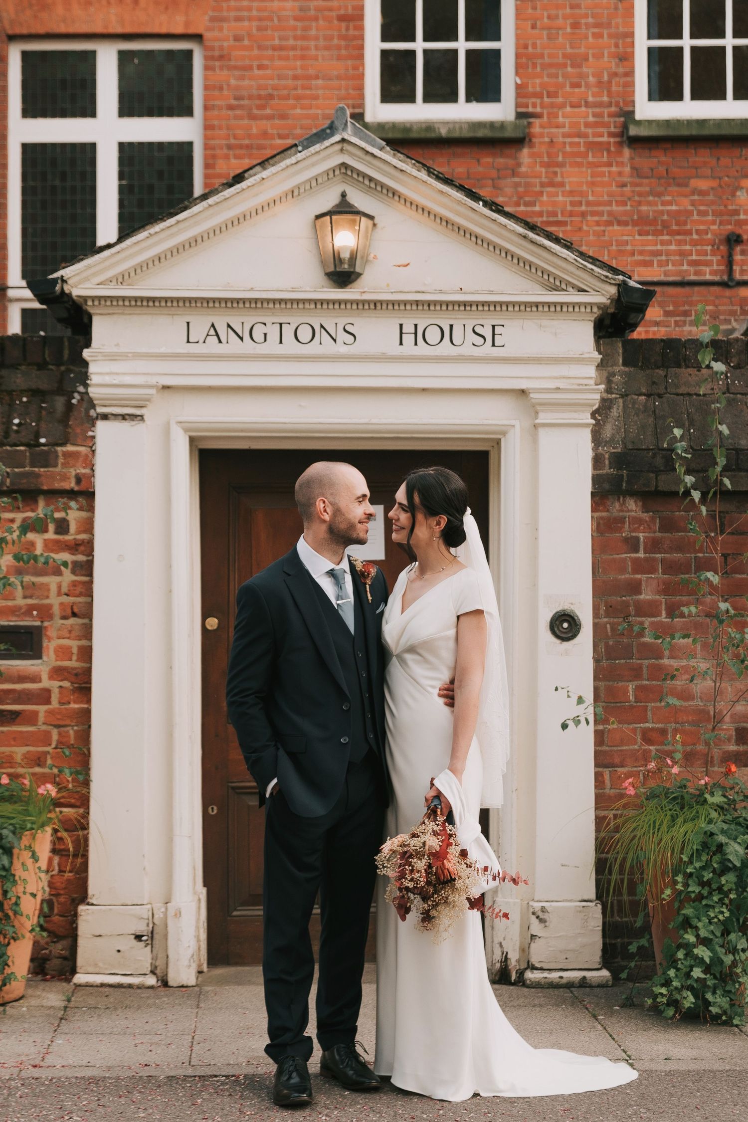 A wedding couple poses for portraits outside a classic brick building with white columns called Langtons House.
