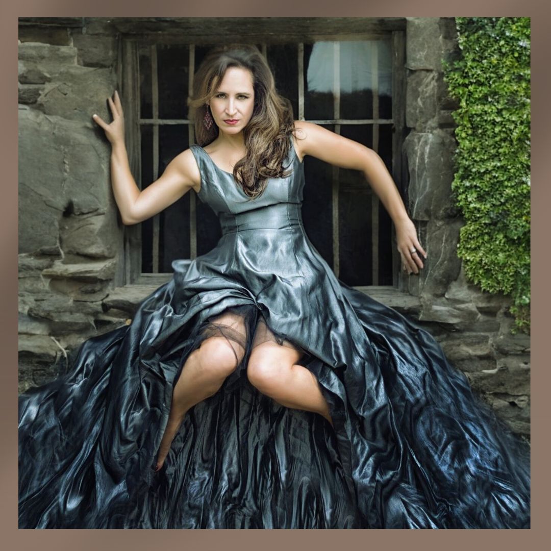 Elegant woman in a dramatic silver and black gown posing dramatically in a stone building doorway.