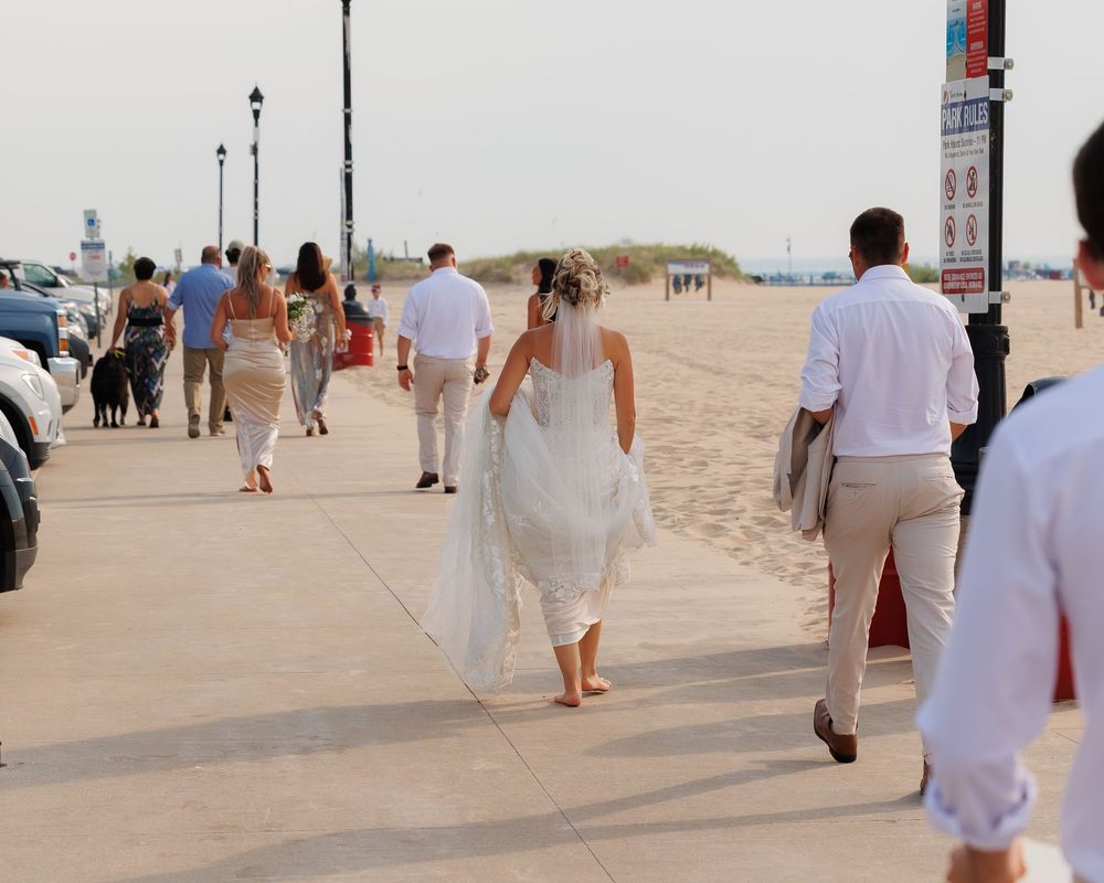 Wedding guests in white attire walking along a sandy beach path during a beach wedding ceremony.