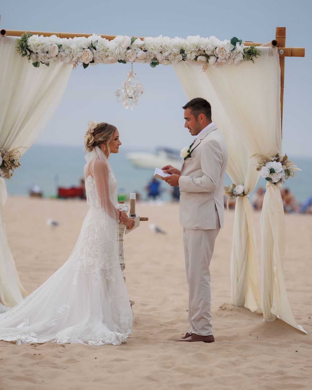 Beach wedding ceremony setup with white floral arch and flowing fabric decorations.