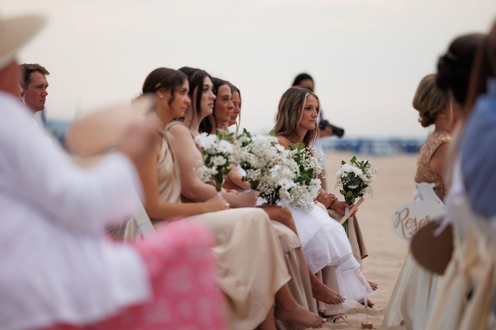 Wedding guests gathered on a beach during a seaside ceremony.