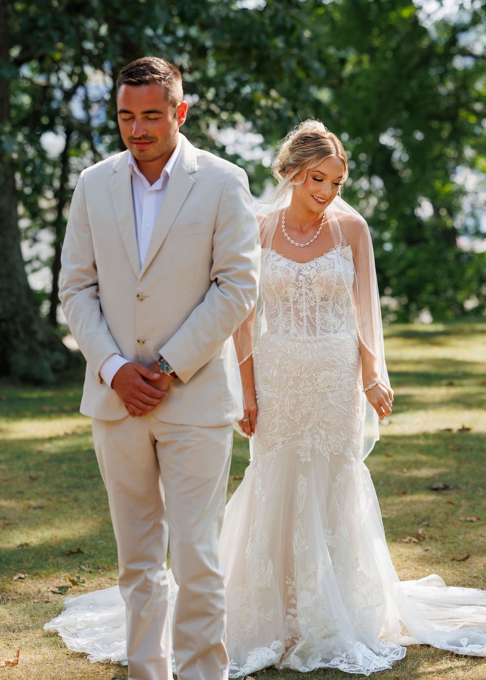 Wedding couple walking together on grassy path in formal attire.