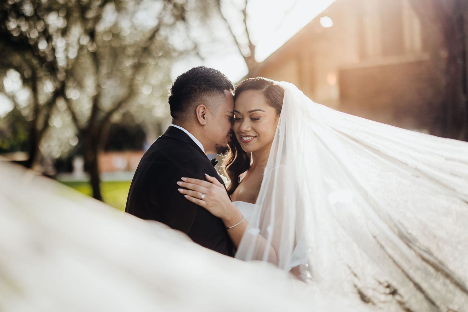 Intimate wedding portrait with flowing veil and golden sunlight.