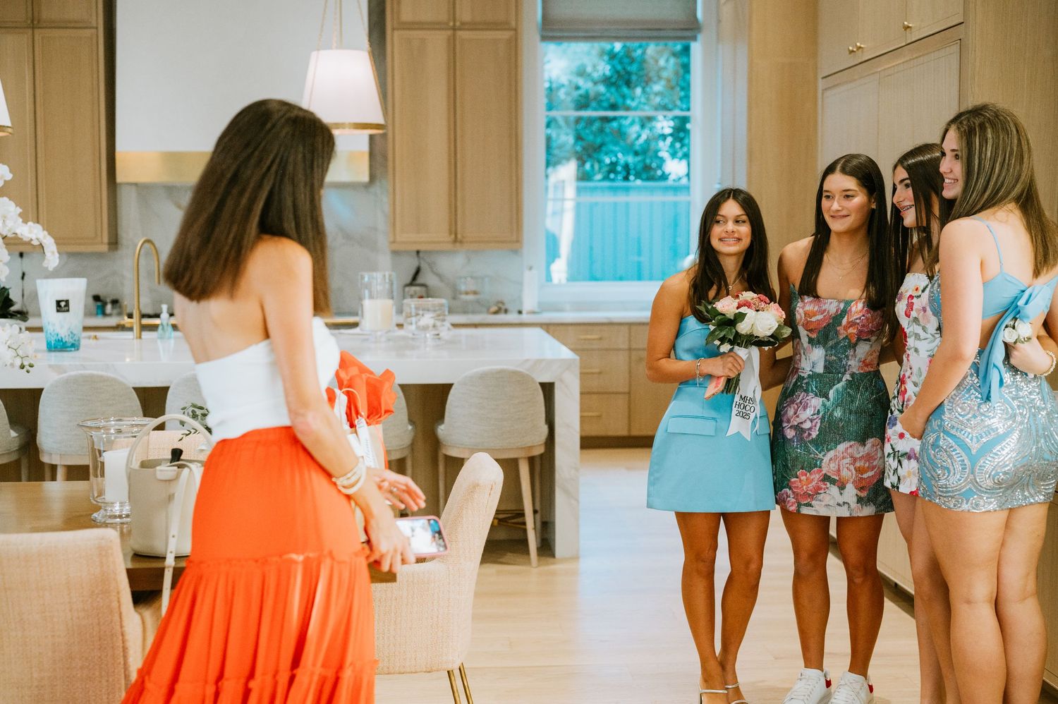 Group of friends in summer dresses gather in a bright modern kitchen for a celebration.