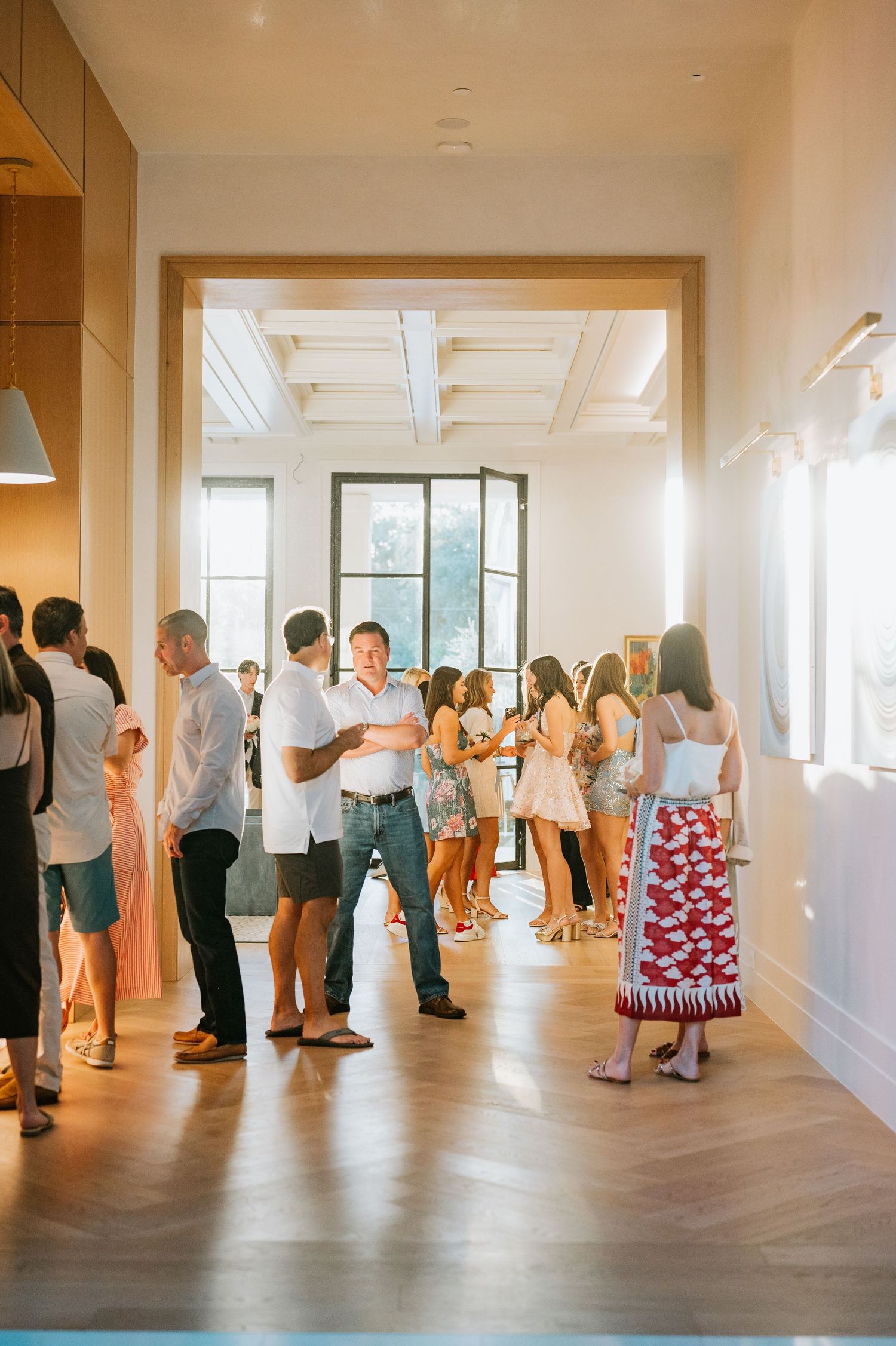 A panoramic view of people mingling in a bright indoor space with hardwood floors and white walls.