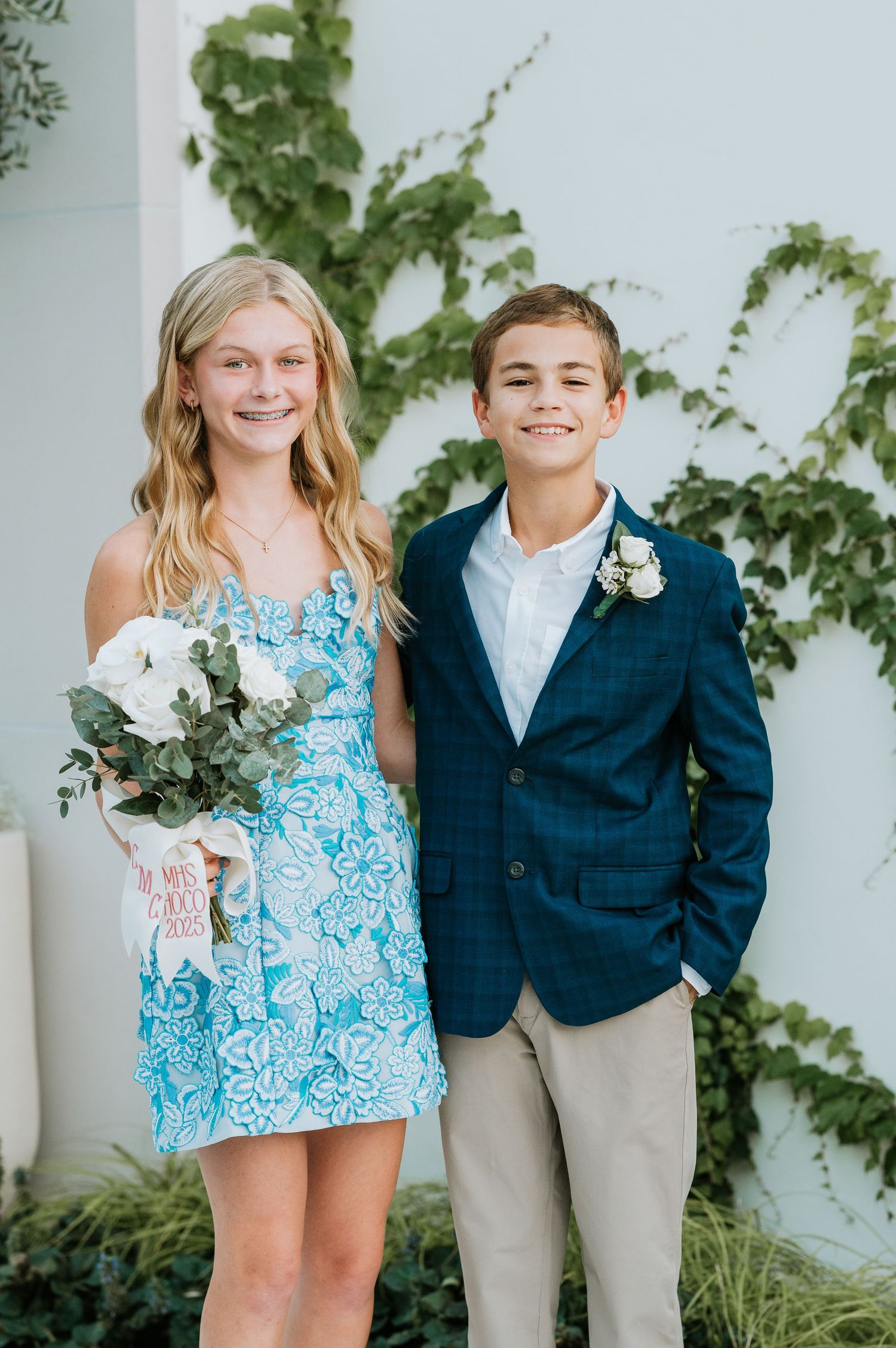 Children in coordinating blue and white outfits pose together against a white wall with climbing vines.