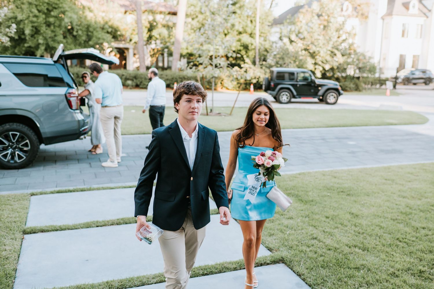 A couple walks together on a grassy lawn during an outdoor celebration in formal attire.
