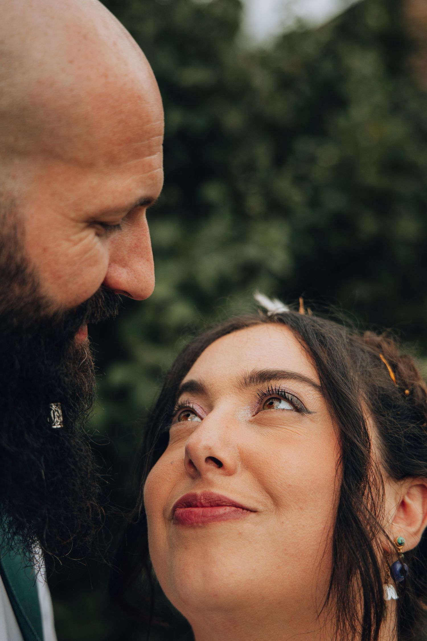Close-up of bride and groom gazing at each other, groom with beard, bride with red lips and floral hair accessory.