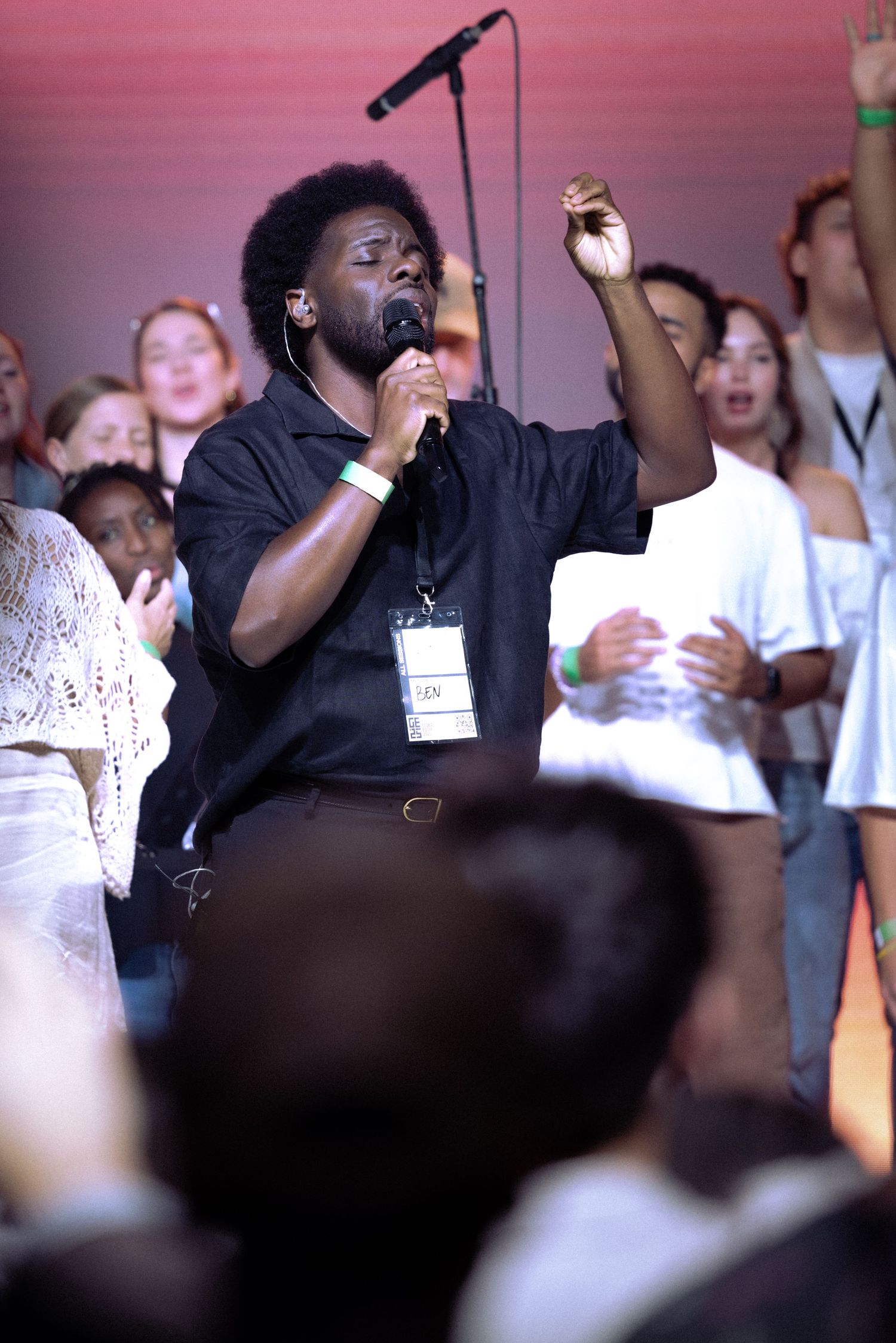 A performer in black attire sings passionately on stage while a crowd watches in the background.