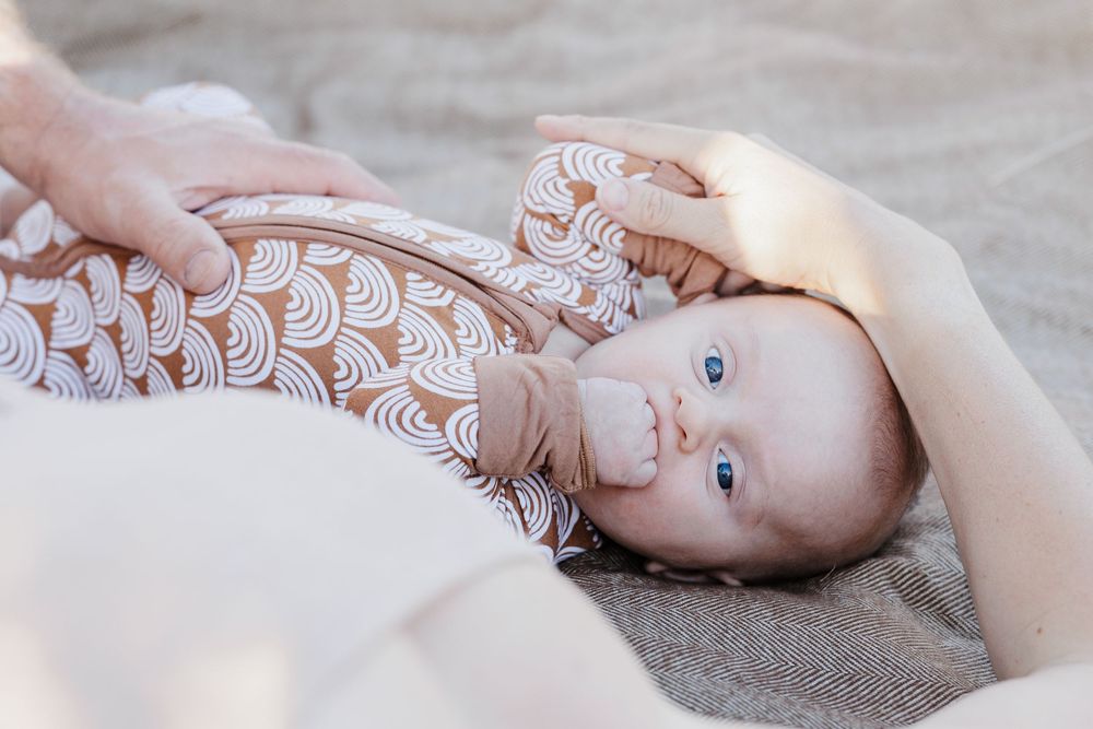 Close-up of blue-eyed baby in patterned onesie lying on textured blanket.