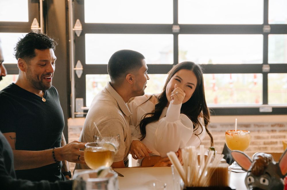 People socializing and enjoying beverages by large windows in a modern restaurant setting.