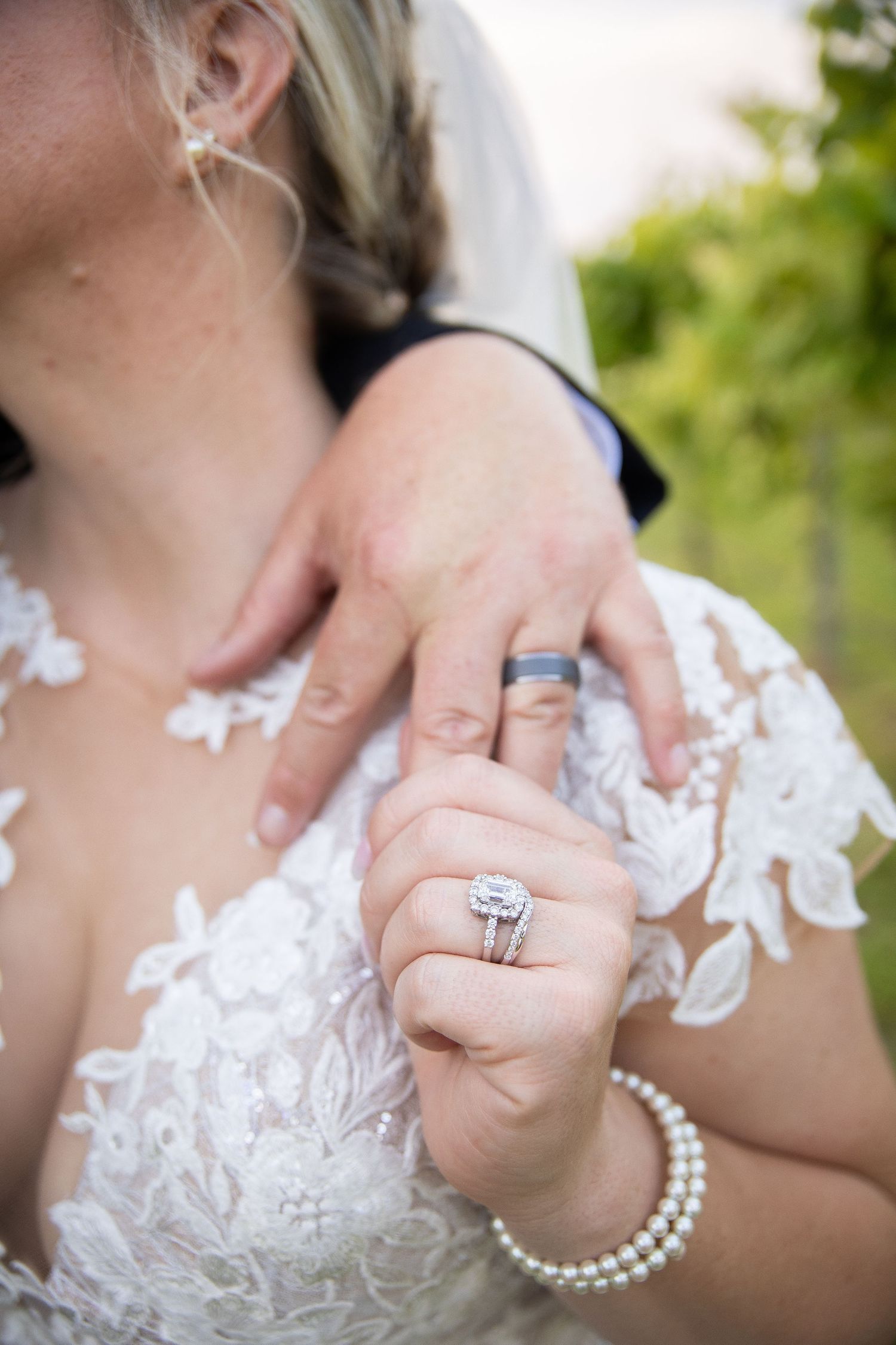Close-up of wedding rings and lace dress details with pearl necklace in elegant bridal photo.