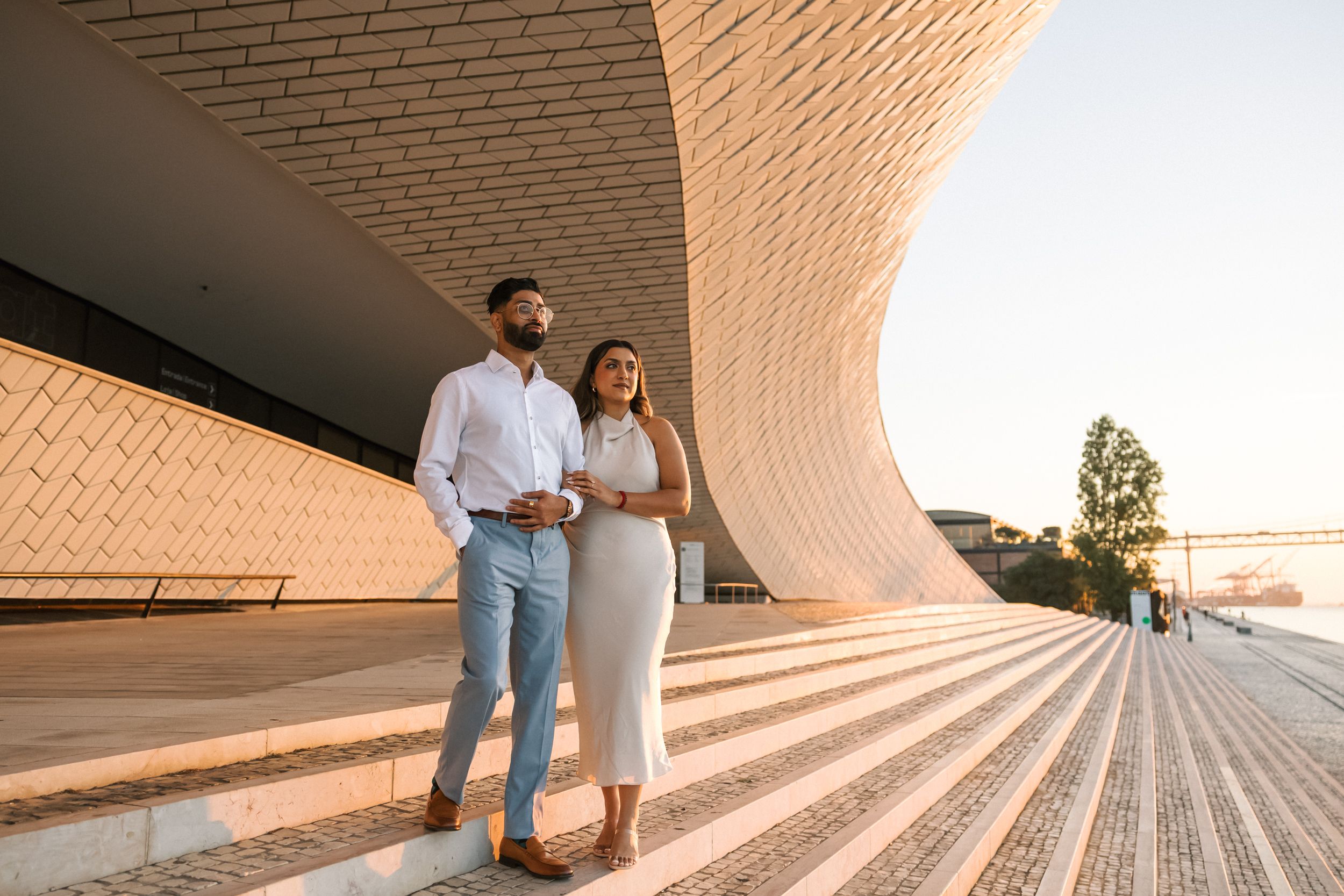 Editorial-style engagement photo at MAAT Museum Lisbon, contemporary architecture and golden morning light. by Portugal Wedding Photographer