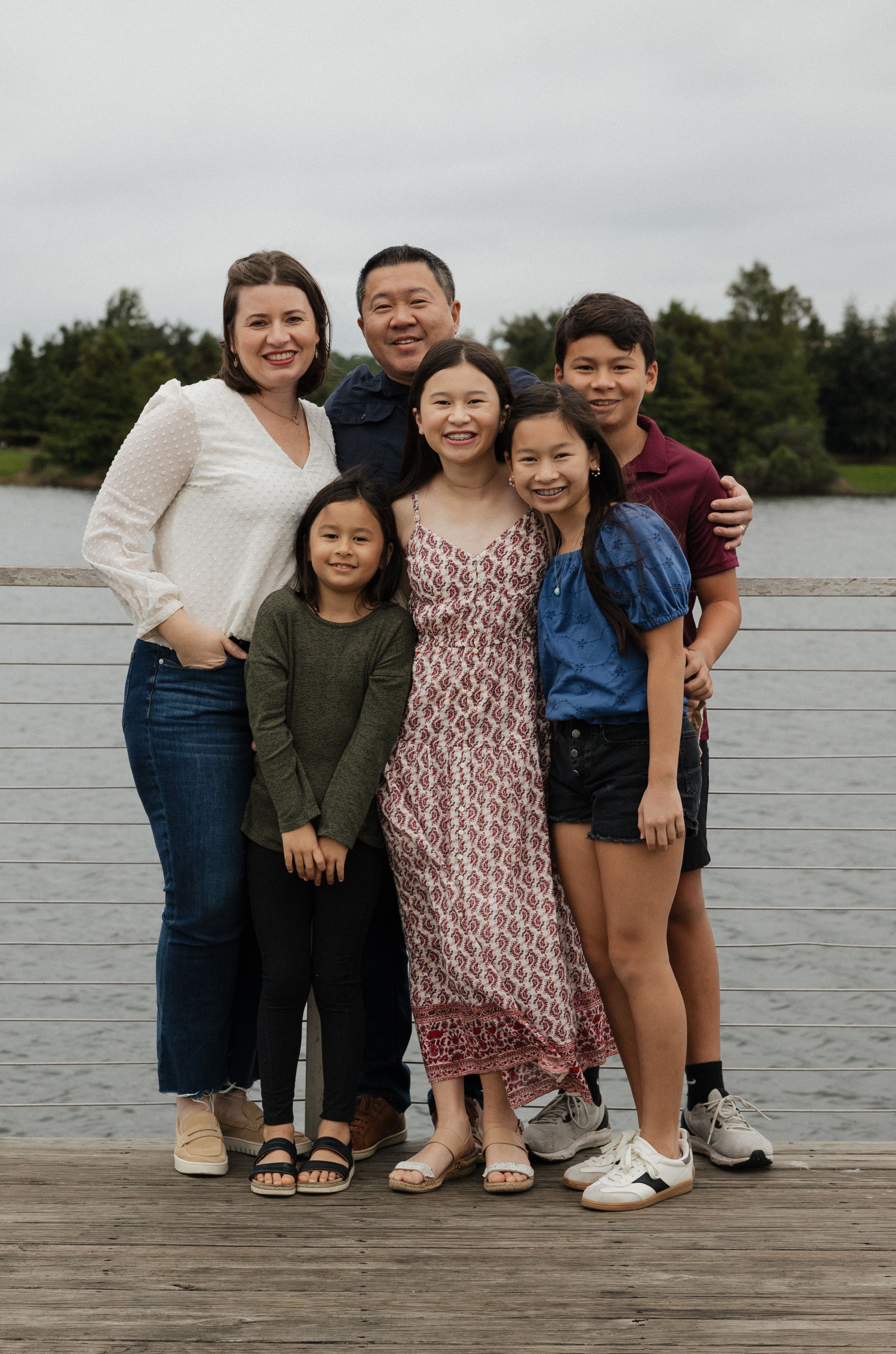 A group poses together on a wooden dock by a lake on an overcast day.