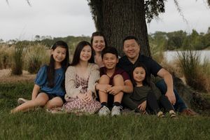 A group sits together under a large tree near a lake on an overcast day.