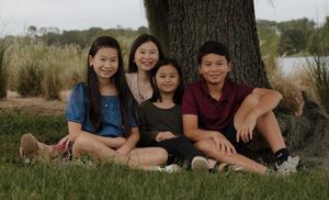 A family group poses together outdoors in casual clothing against a natural backdrop.