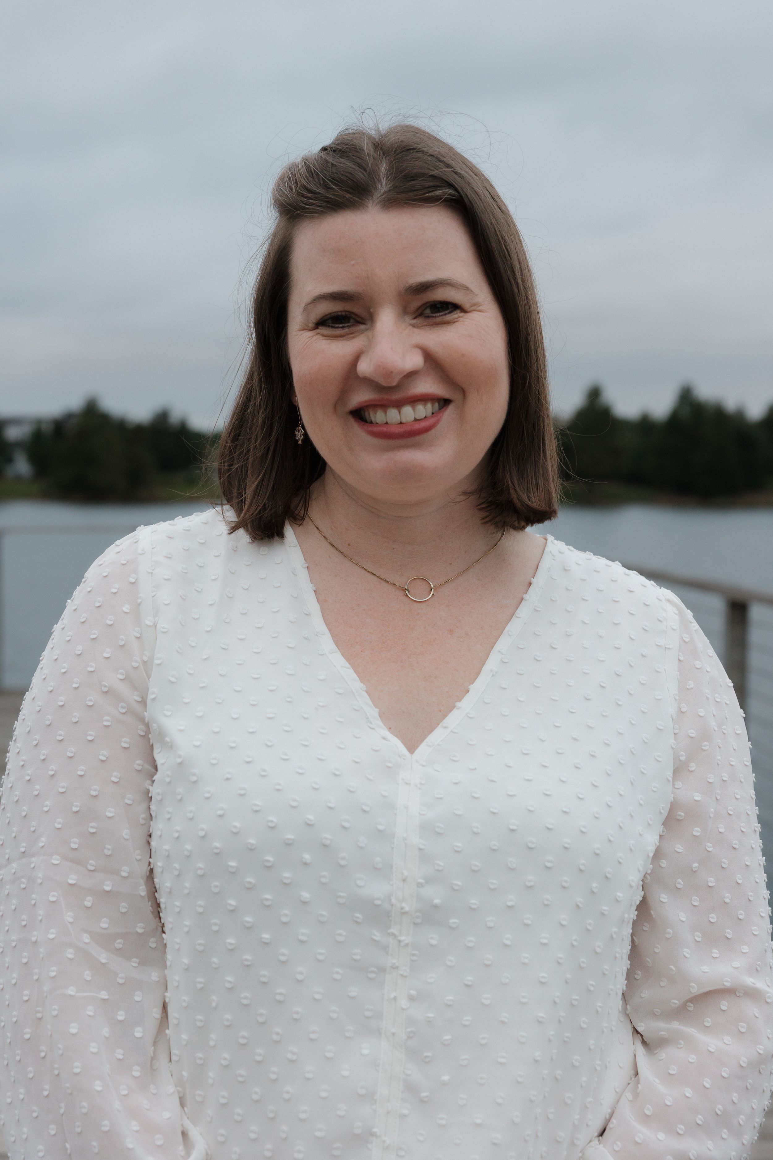 A person in a white textured blouse smiles brightly at the camera.