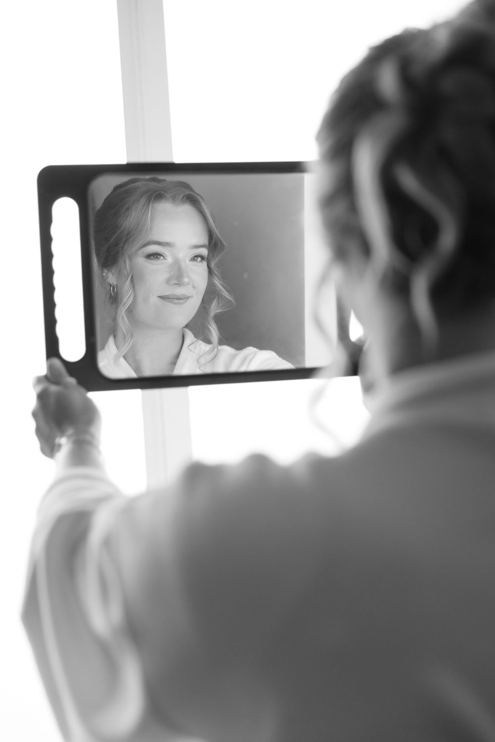 Wedding preparation scene reflected in handheld mirror during bridal styling.