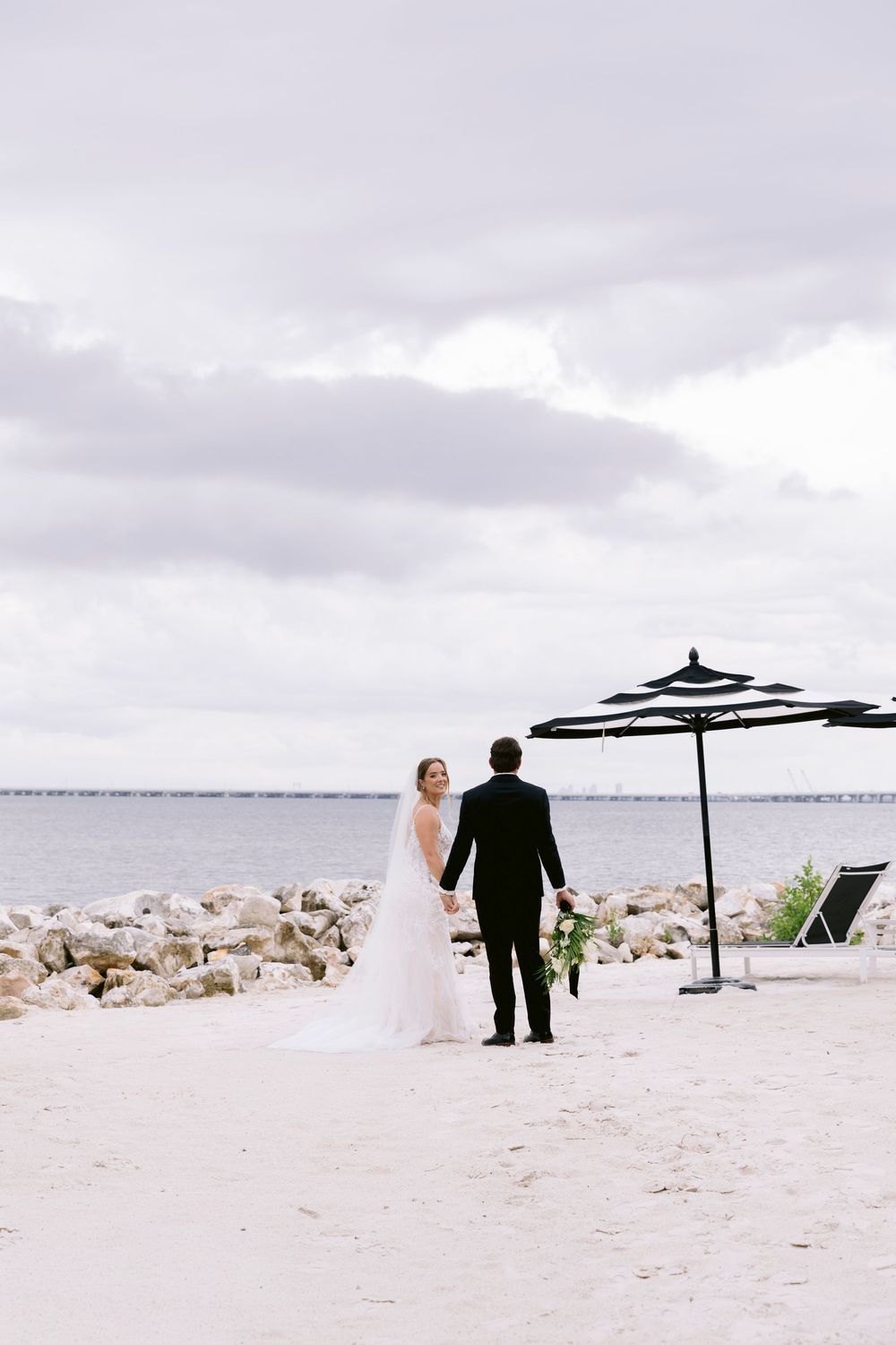 A beach wedding scene with a striped umbrella and white sand overlooking the ocean.