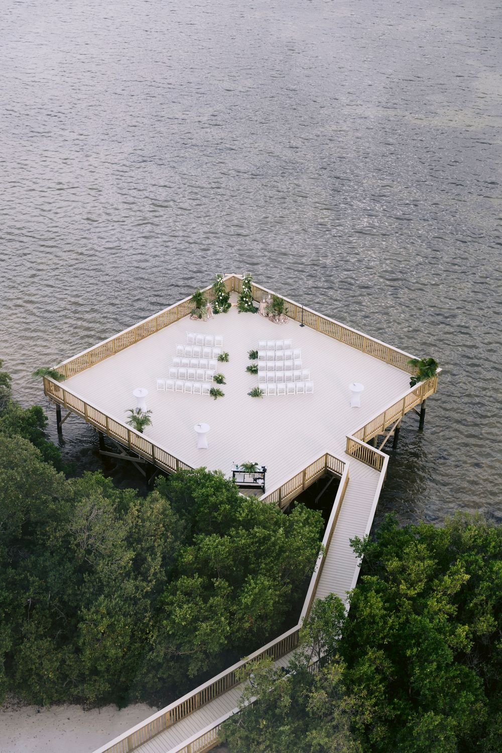 Aerial view of a white triangular deck extending over water surrounded by lush greenery.