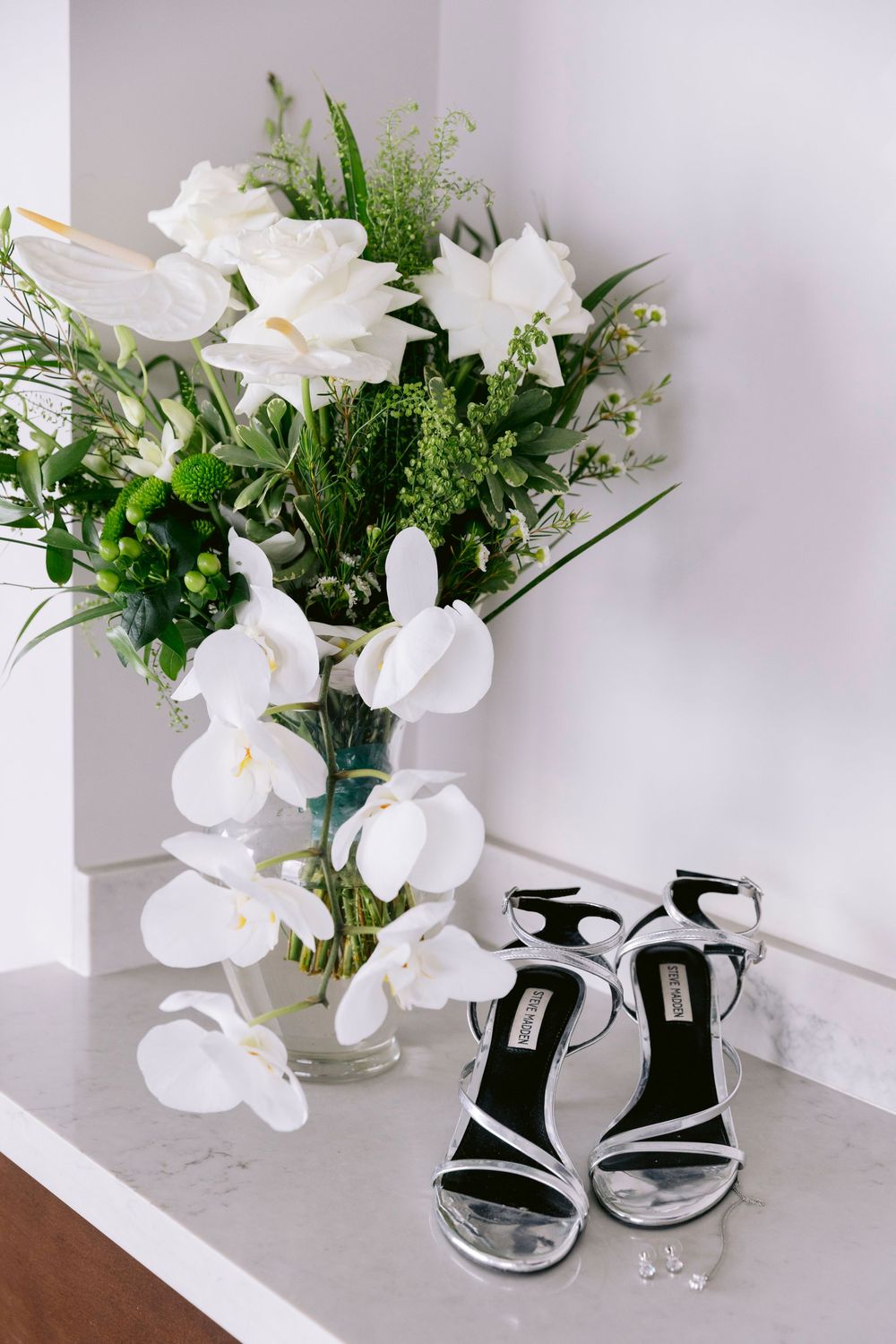 Elegant bridal accessories with white orchid bouquet and black heels against light background.