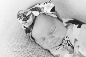 Black and white photo of a sleeping newborn baby wrapped in soft blankets with a delicate bow headband.