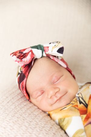 A sleeping baby wearing a floral headband rests peacefully on a white textured surface.