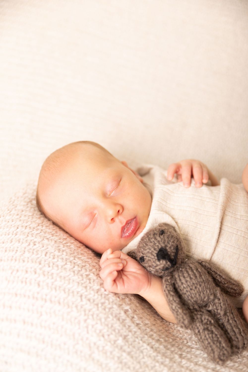 A sleeping newborn wearing a cozy gray knit hat rests peacefully on soft white textured bedding.