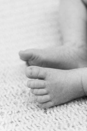 Close-up black and white photo of tiny baby feet resting on textured knit fabric.