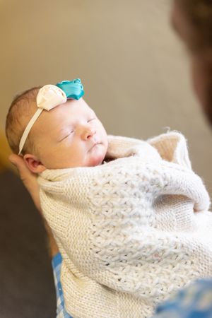 A sleeping newborn baby wrapped in a white knitted blanket rests peacefully against a neutral background.