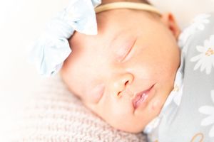 A sleeping newborn baby wrapped in soft white fabric rests peacefully against a light background.