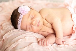 Peaceful newborn baby sleeping on soft pink blankets in a delicate and serene pose.