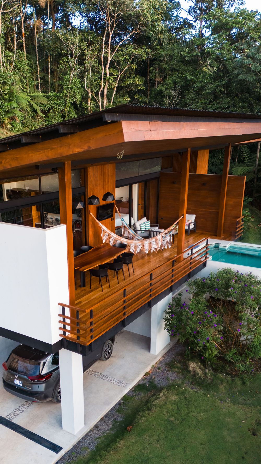 Modern wooden house with carport and pool nestled in tropical forest setting.