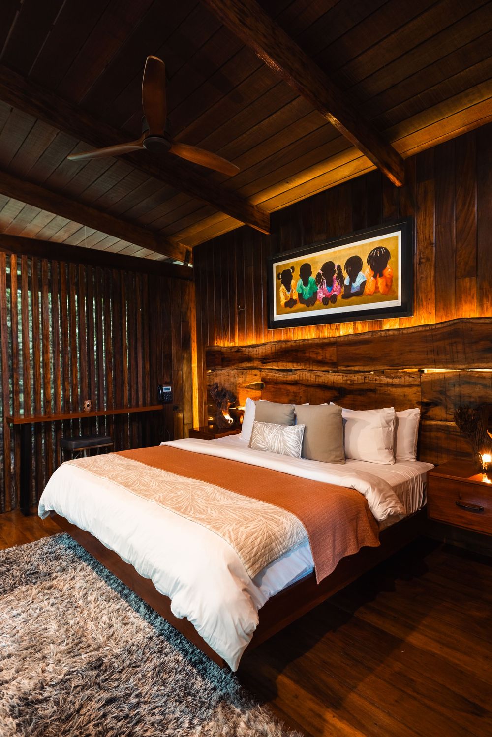 Cozy bedroom with wood-paneled walls featuring colorful wall art and plush bedding.