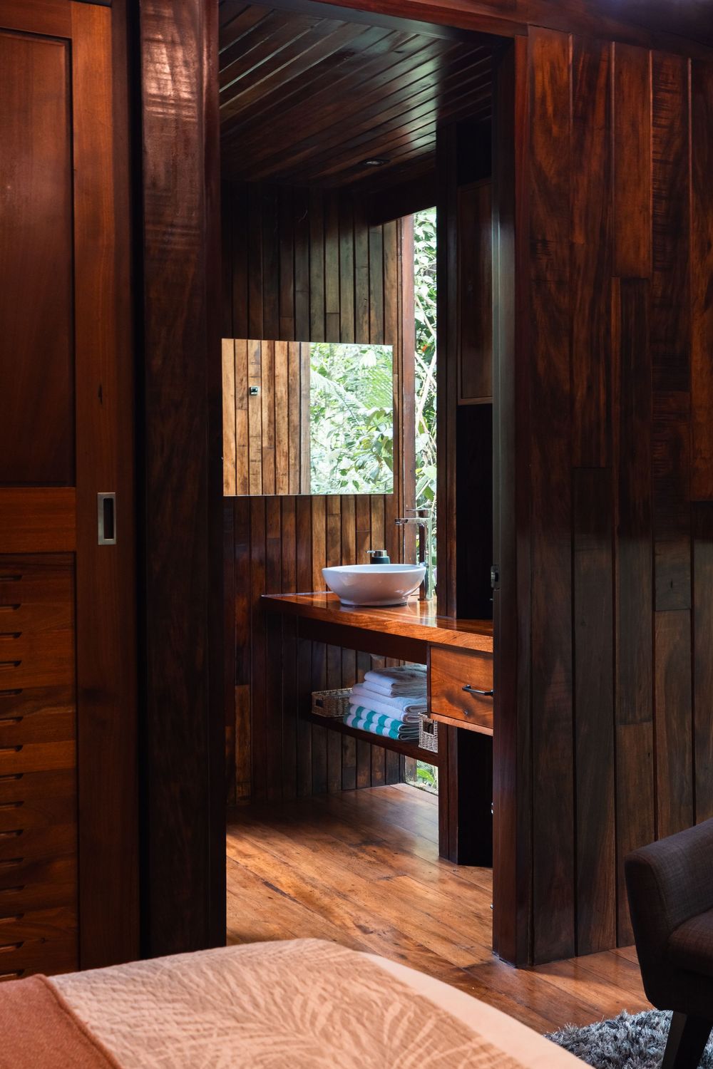 Natural light streams through windows in dark wood-paneled cabin bedroom.