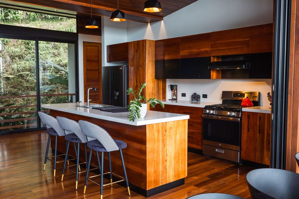 Modern kitchen and dining area with warm wood paneling, pendant lights, and sleek black bar stools.