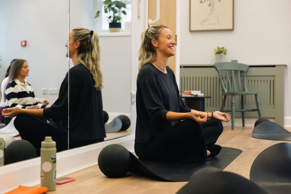 Group fitness class participants sitting on floor in bright studio space.