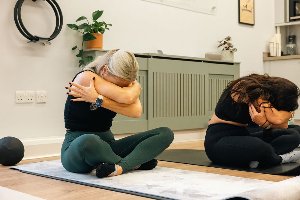 Exercise class participants doing floor stretches on yoga mats in bright studio.