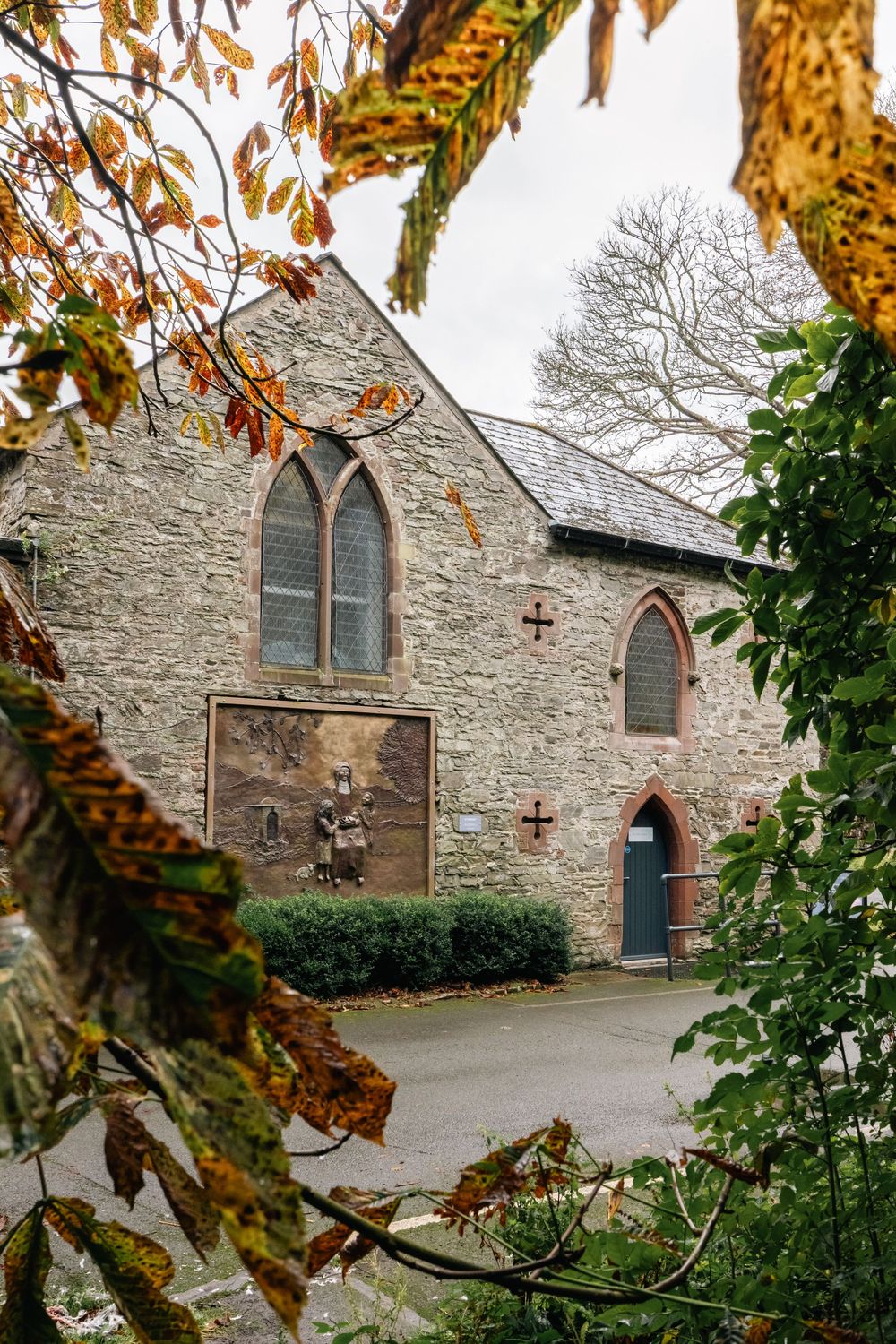Stone church building with Gothic windows framed by autumn leaves.