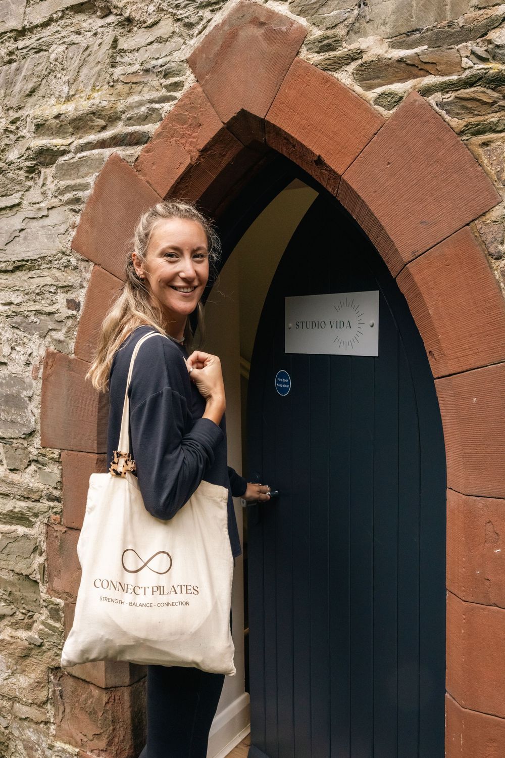 Person carrying tote bag entering through arched stone doorway.