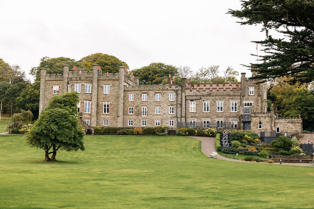 Panoramic view of a historic stone mansion set on sprawling green grounds.