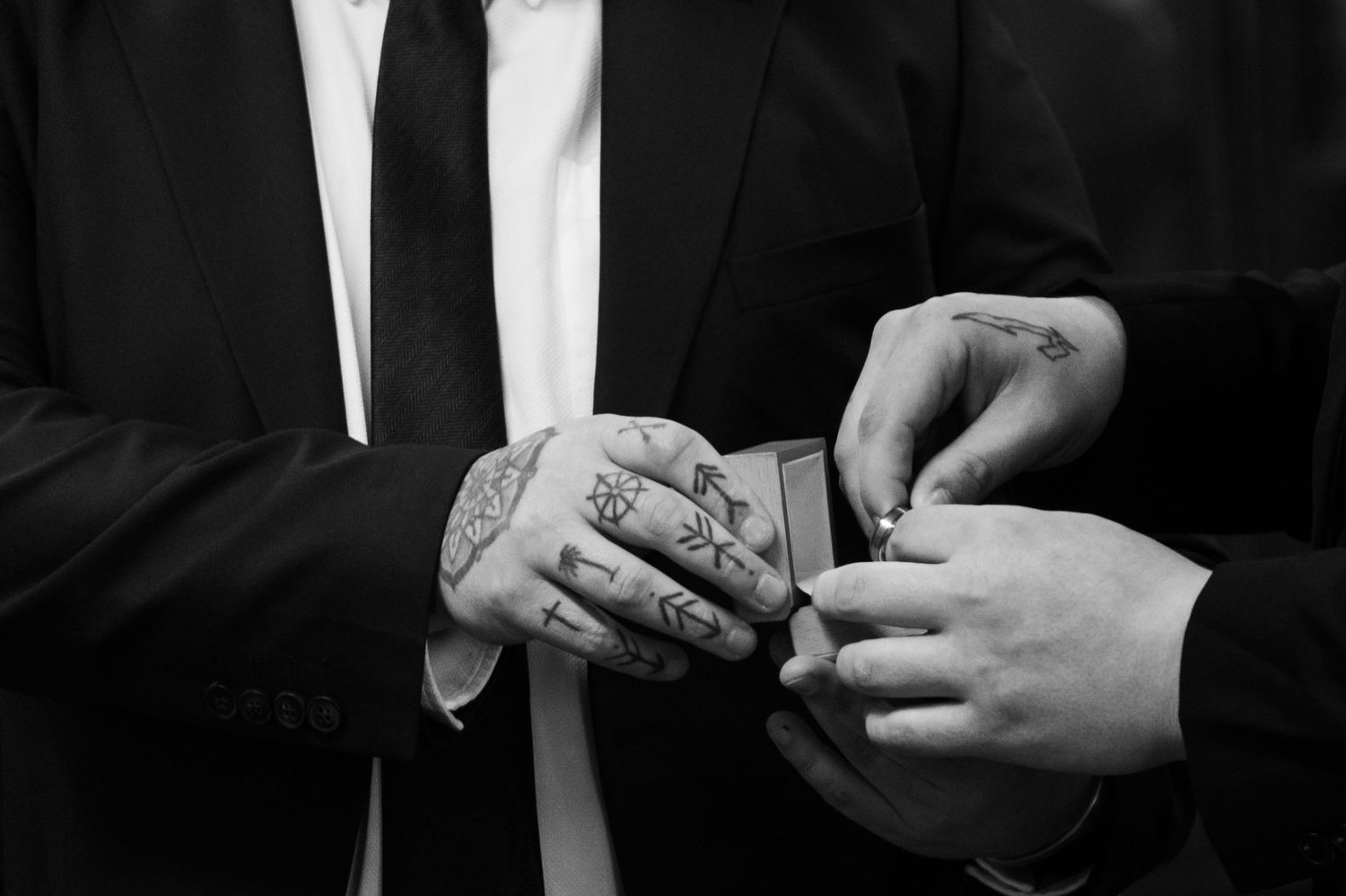 Black and white close-up of hands exchanging wedding rings during ceremony.