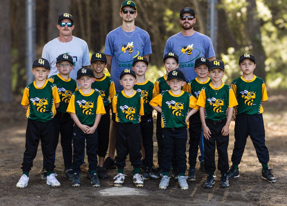 Youth baseball team in green and yellow uniforms posing with coaches in forest setting.