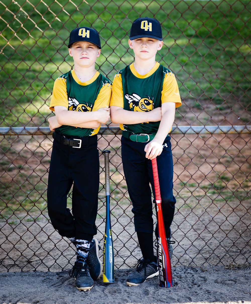 Two baseball players in matching yellow and navy uniforms leaning against chain-link fence.